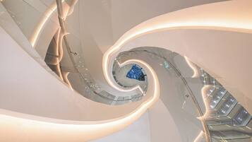 A spiral staircase with glass railings and a central blue geometric structure.