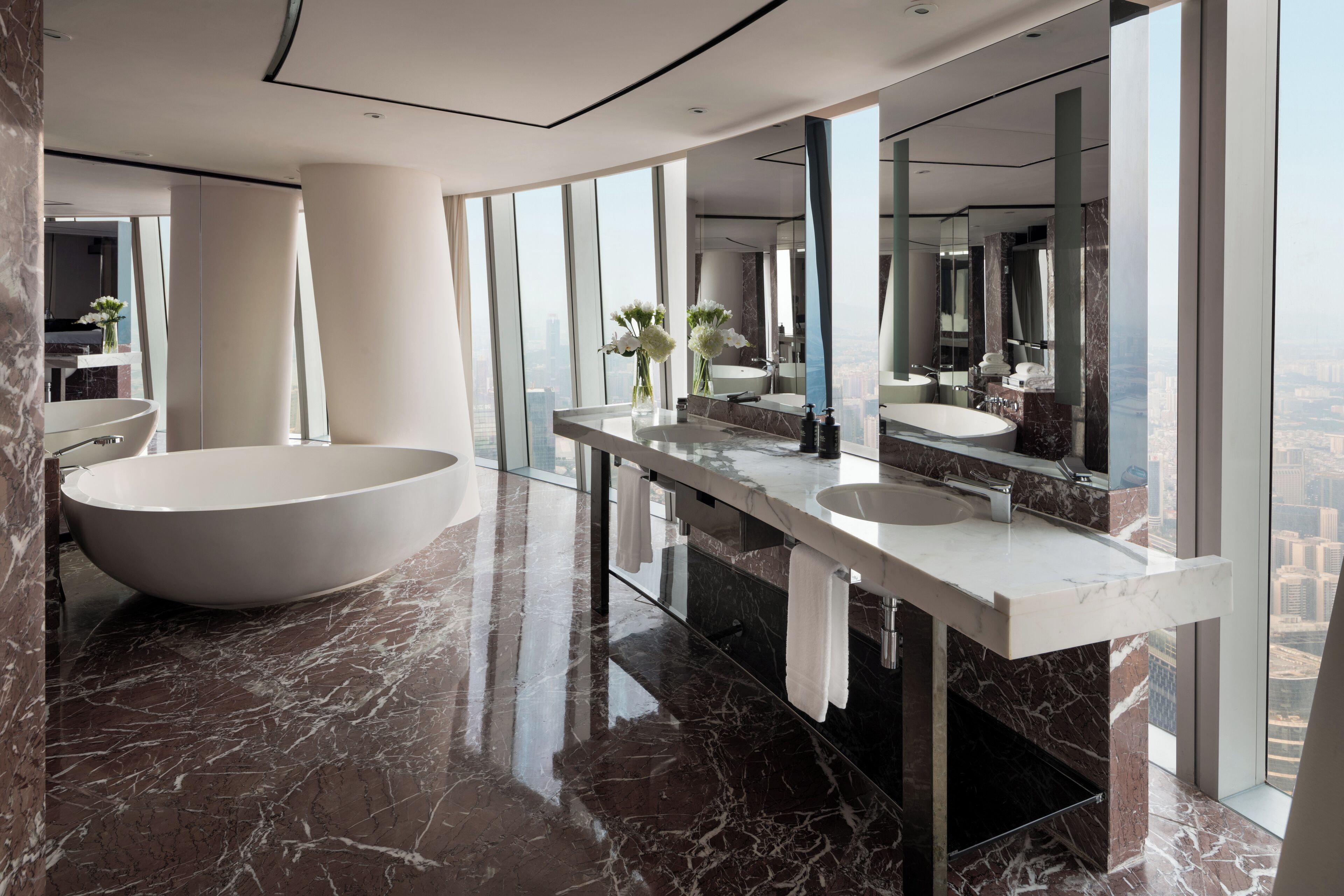 Un bagno moderno con una vasca da bagno indipendente, un mobile vanitario con specchio e vista sulla città attraverso ampie finestre.