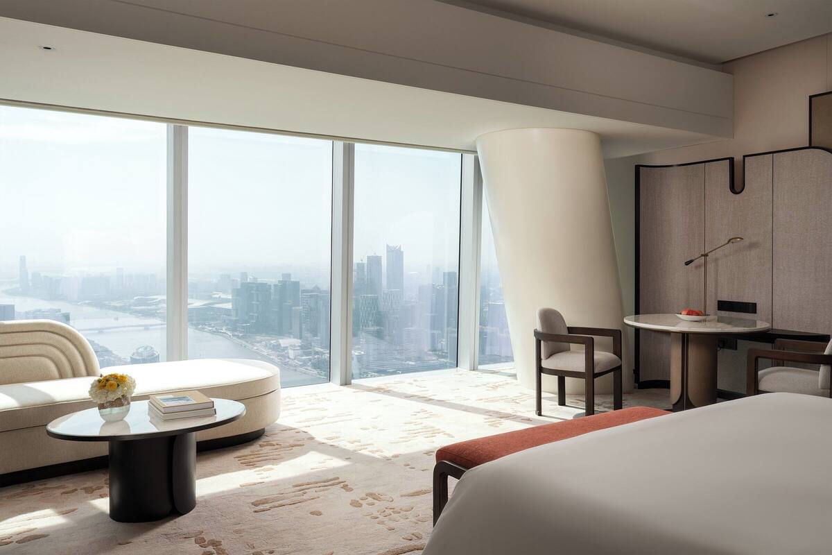 A modern hotel room with a large window, a round table, a sofa, and a bed.