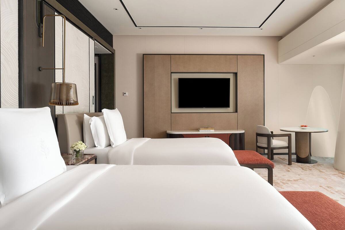 Moderni hotellihuone, jossa on kaksi sänkyä, televisio, pieni pöytä ja tuoli.