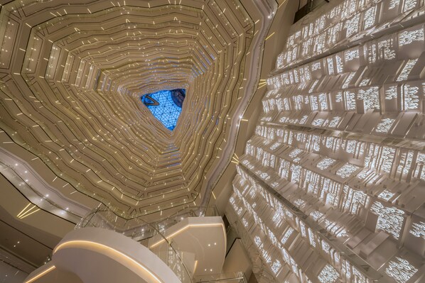 A modern architectural interior with a central atrium, multiple levels, and a geometric ceiling design.
