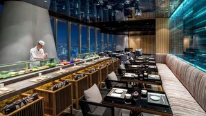 A modern restaurant with a sushi bar, seating area, and city views.