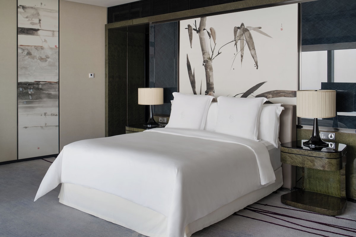 A modern hotel room with a large bed, two bedside tables, and a wall-mounted artwork.