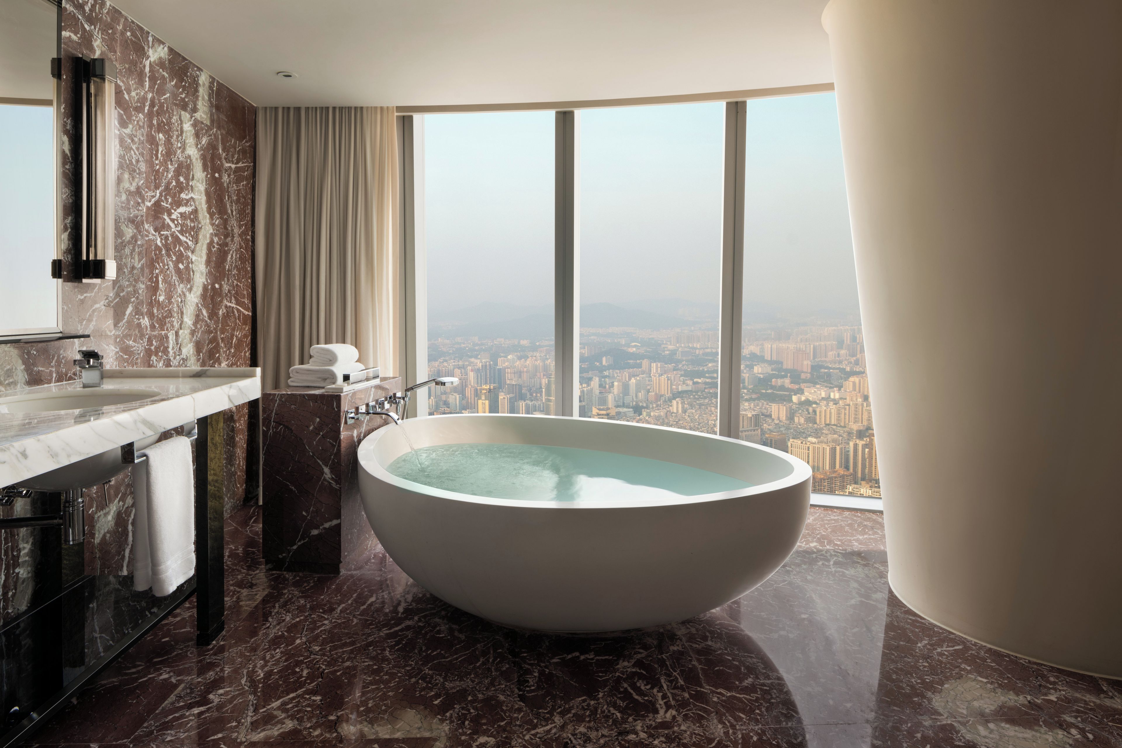Un baño moderno con una bañera independiente, paredes de mármol y vistas a la ciudad.