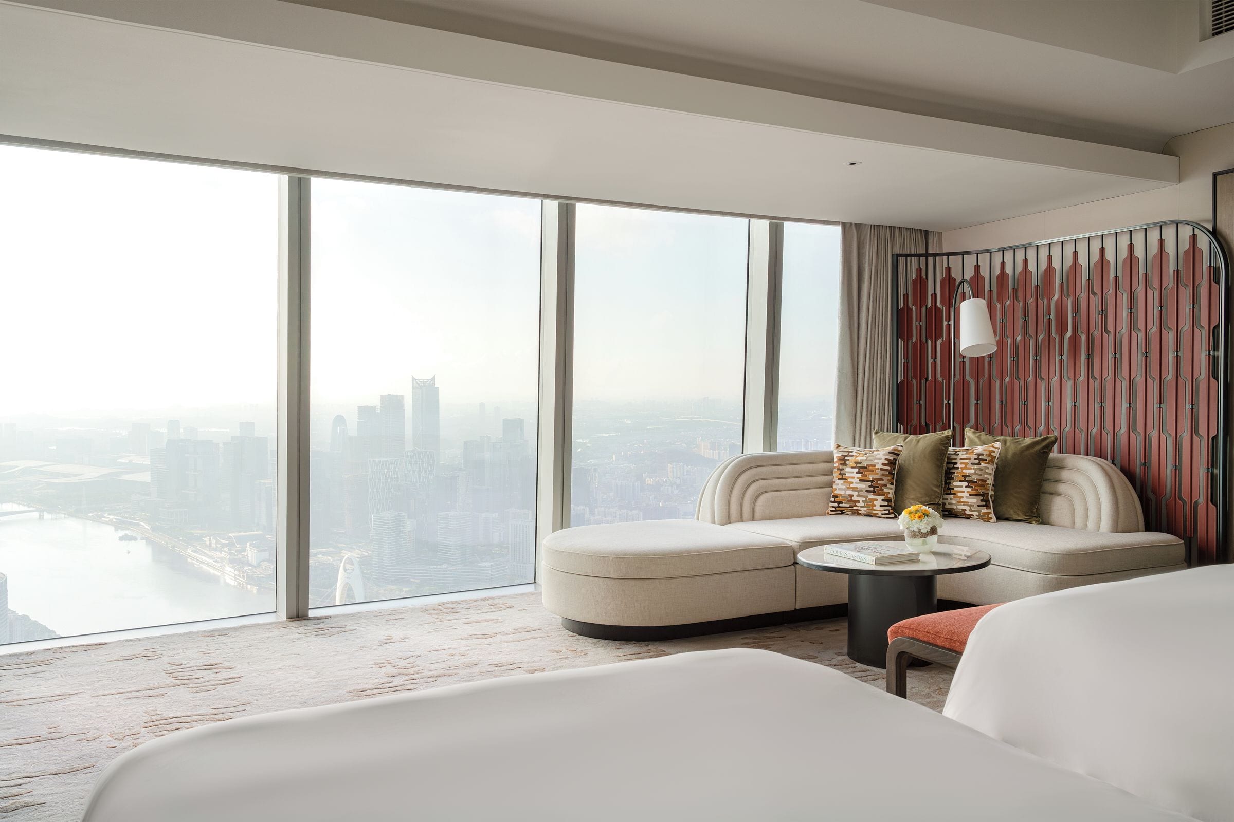 Habitación de hotel moderna con una amplia vista de la ciudad, un sofá, una mesa redonda de centro y una cama.