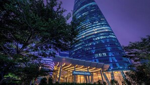A tall, modern hotel with a distinctive curved design, featuring a prominent entrance and illuminated windows.