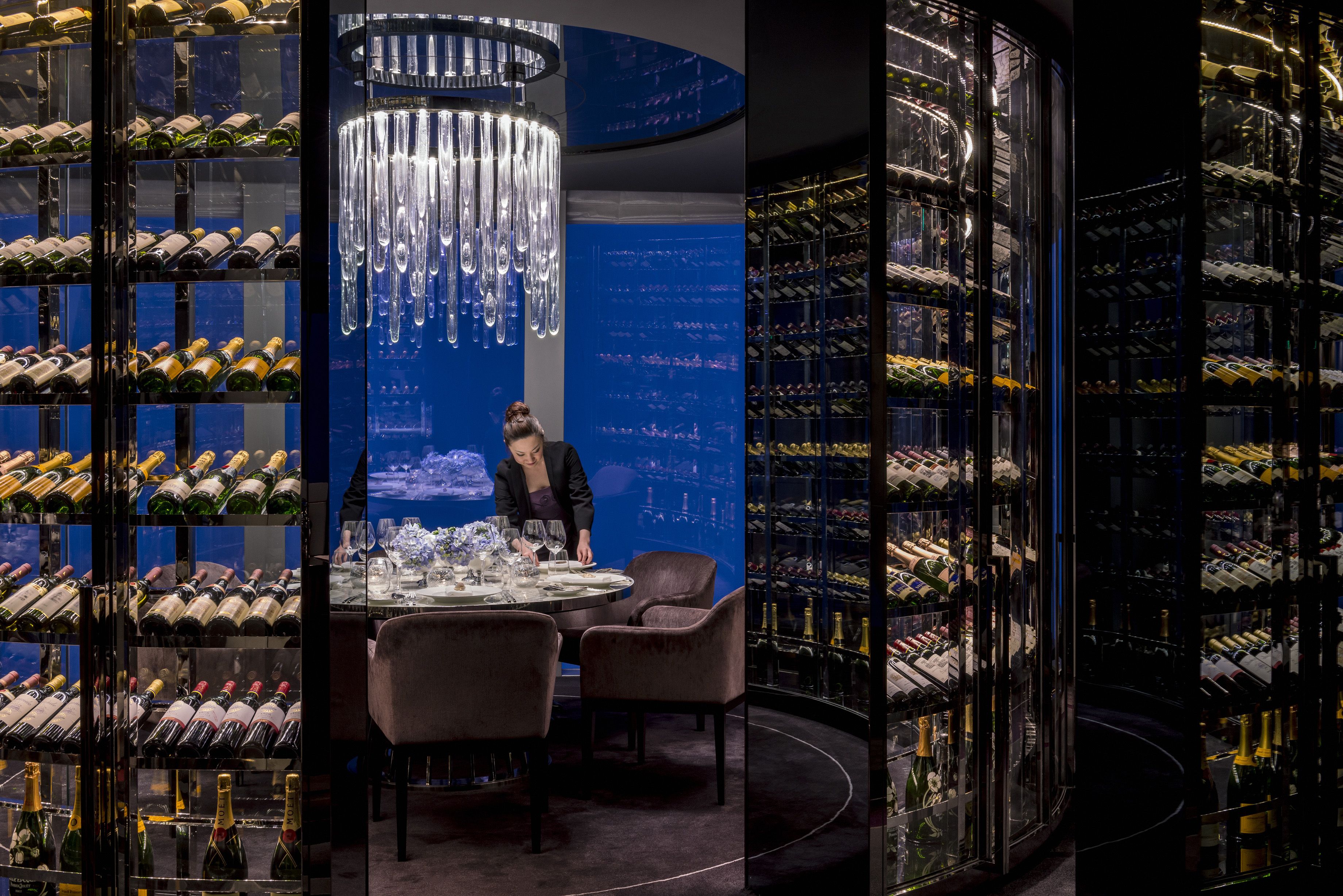 A wine cellar with a round table and chairs, surrounded by shelves of wine bottles.