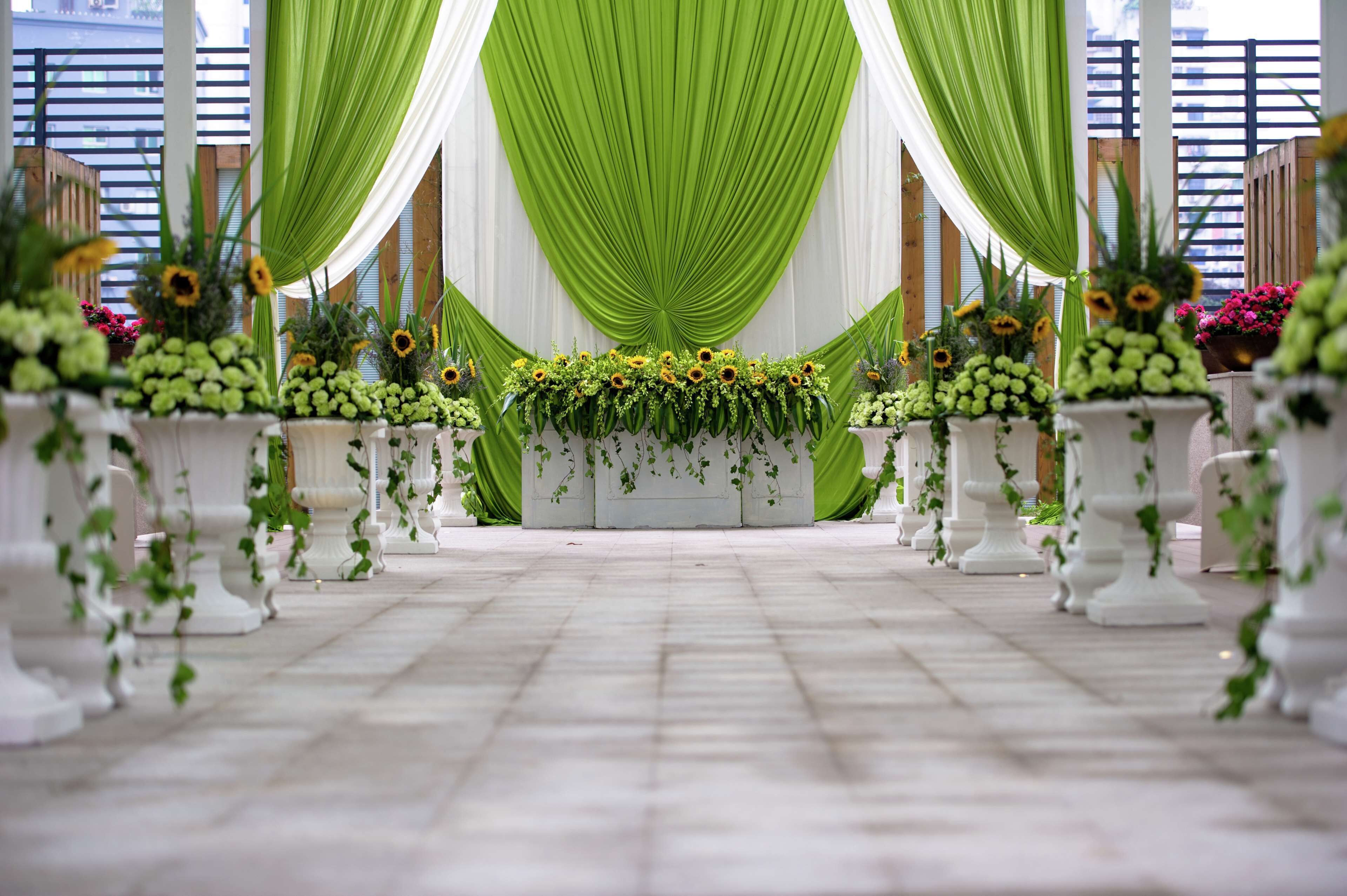 A ceremonial aisle with white columns, green drapes, and floral arrangements.
