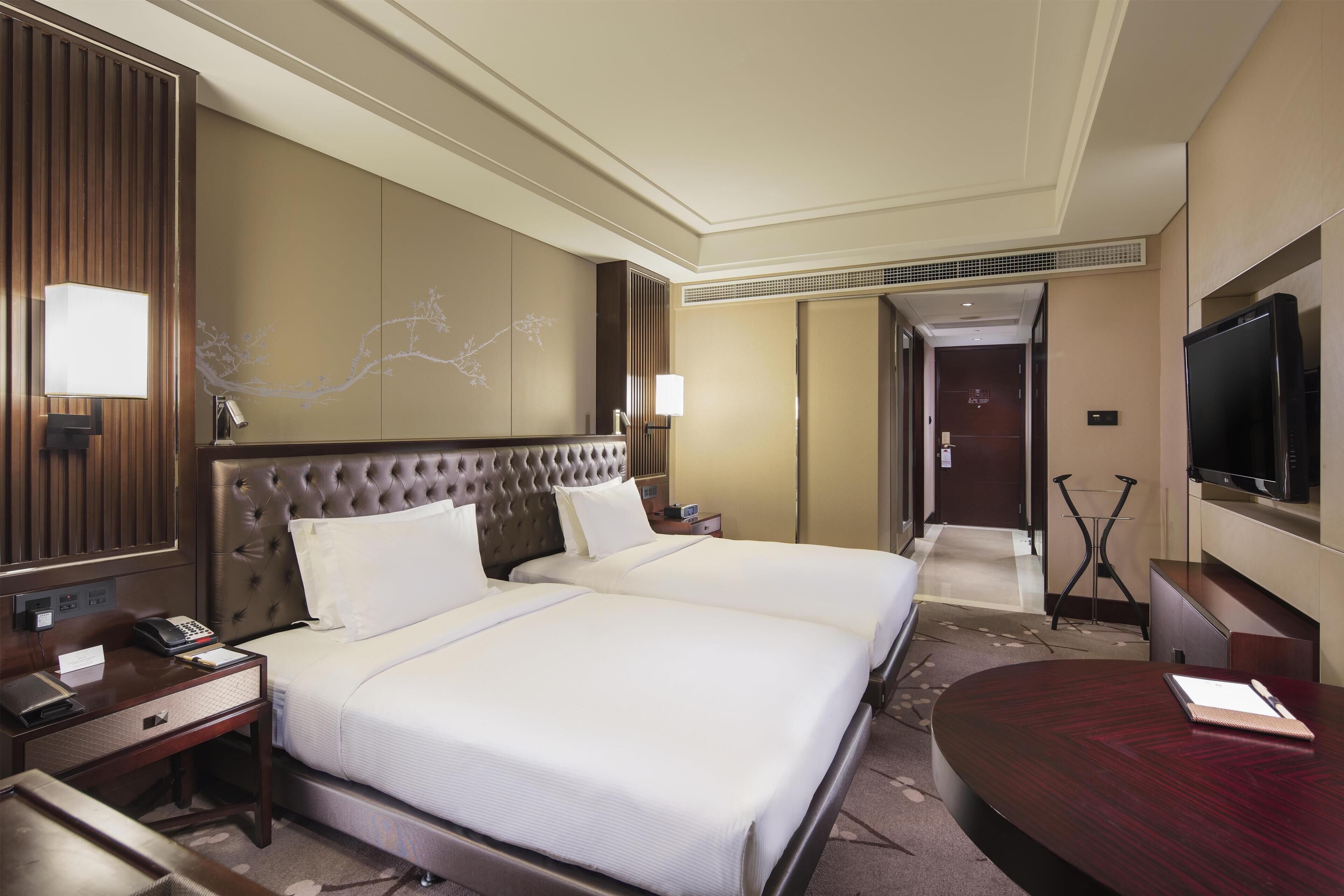 Une chambre d’hôtel dotée d’un grand lit, de tables de chevet, d’un bureau, d’un téléviseur à écran plat et d’un téléviseur fixé au mur.