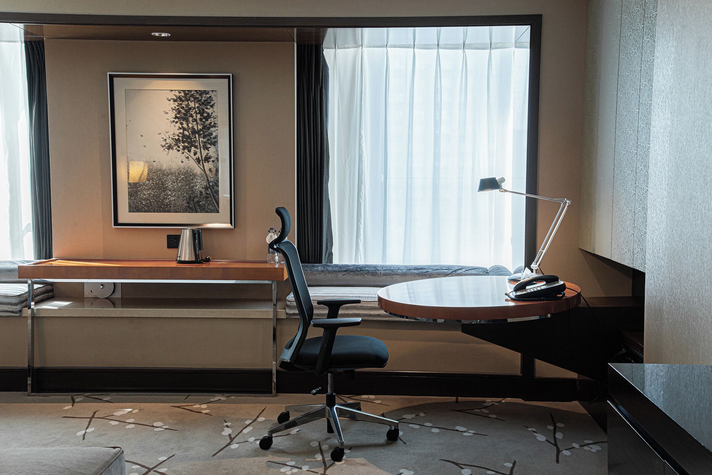 Habitación de hotel con escritorio, silla y un ventanal con cortinas.