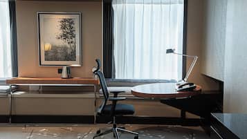 Ein Hotelzimmer mit Schreibtisch, Stuhl und einem großen Fenster mit Vorhängen.