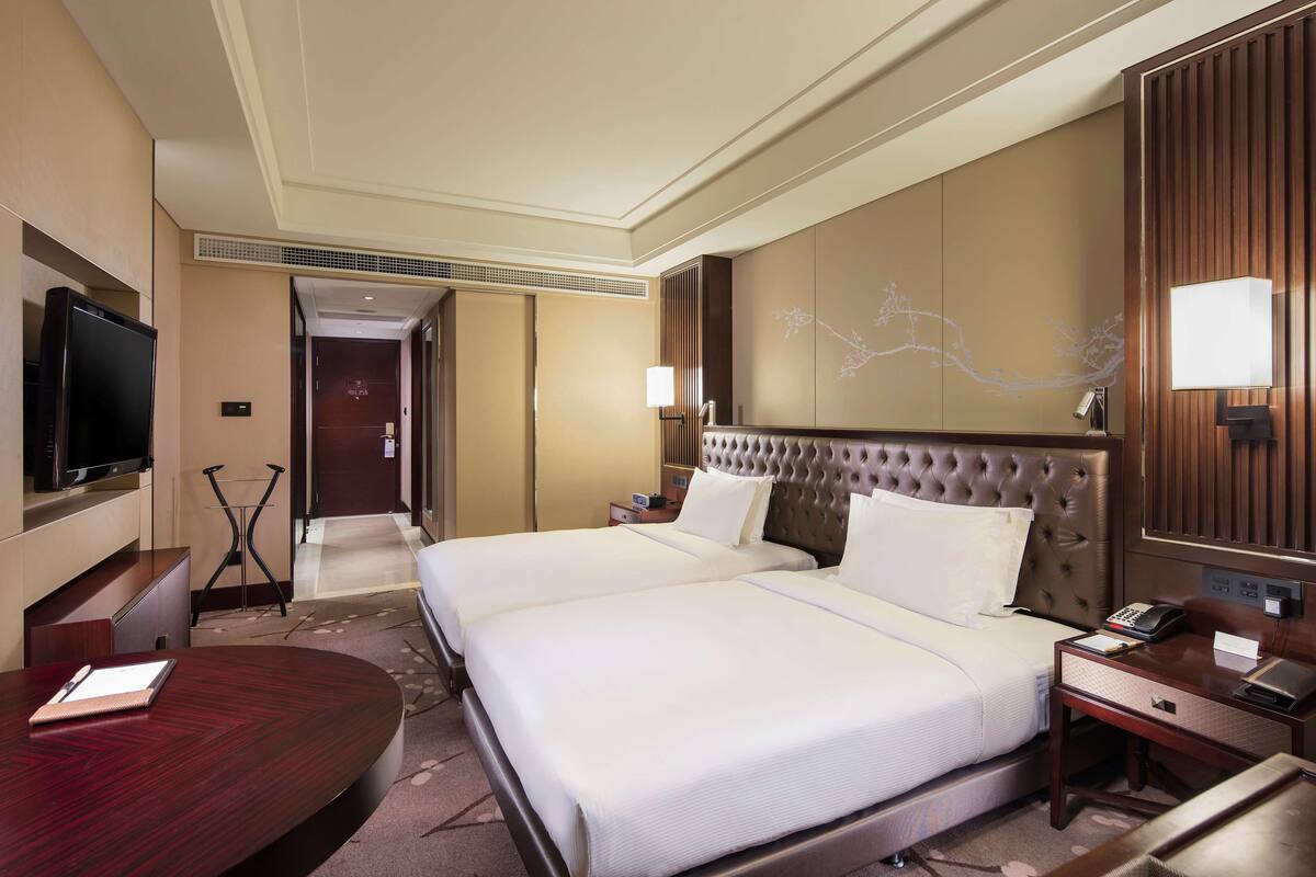 Ein Hotelzimmer mit zwei Betten, einem Fernseher, einem Schreibtisch und einer Lampe.