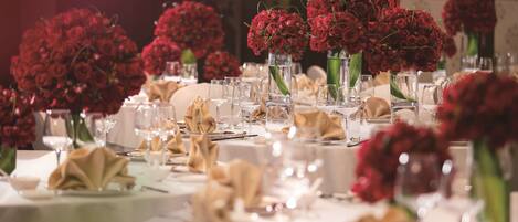 A table set for a formal event with red flowers in vases, clear glassware, and folded napkins.