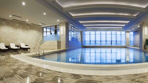 Una amplia piscina cubierta con suelo de baldosas, barandilla de cristal y zona de estar con sillones reclinables.