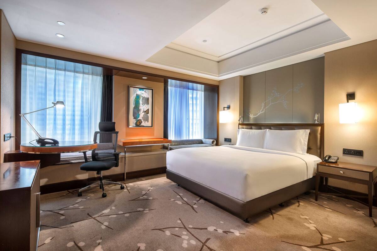Ein Hotelzimmer mit einem großen Bett, einem Schreibtisch mit Lampe, einem Sessel und einem Nachttisch mit Telefon.