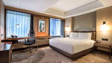 A hotel room with a large bed, a desk with a lamp, a chair, and a nightstand with a phone.