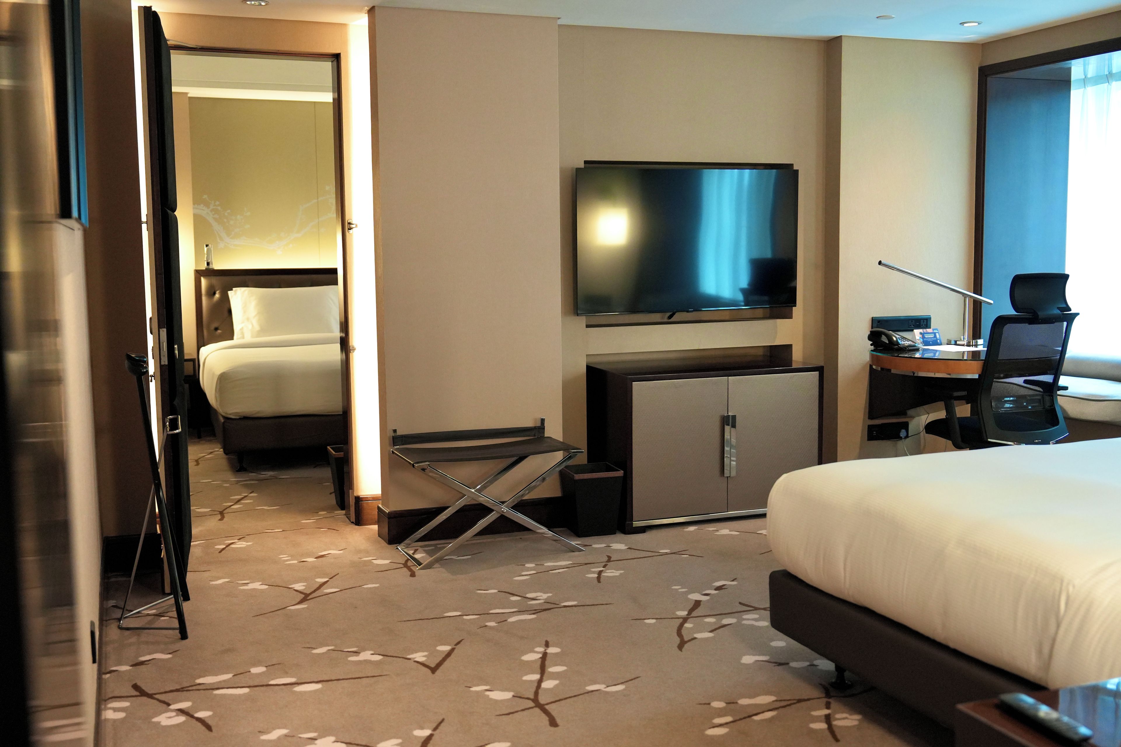 Una habitación de hotel con una cama, un escritorio con una silla, un televisor y un minibar.