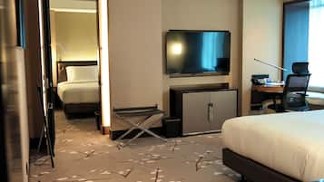 Una habitación de hotel con una cama, un escritorio con una silla, un televisor y un minibar.