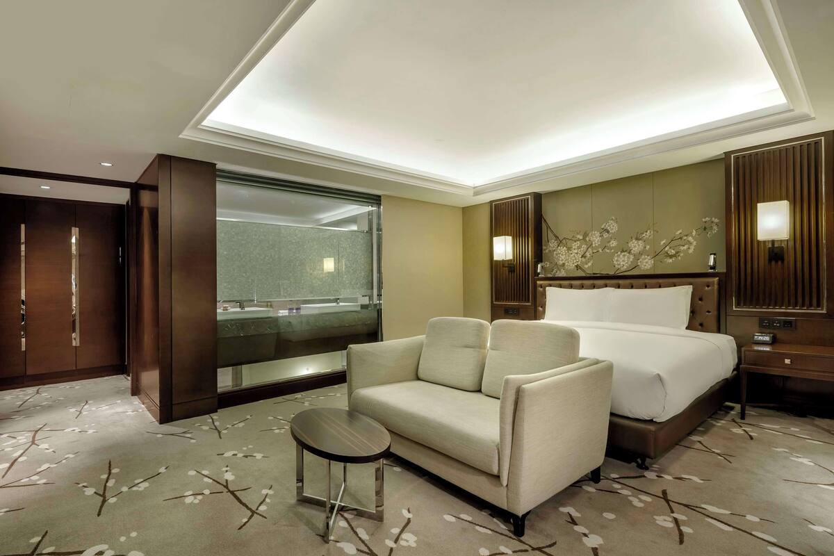 Ein Hotelzimmer mit Bett, Sofa, kleinem Tisch, Nachttisch, Spiegel, Fenster und Duschbereich.
