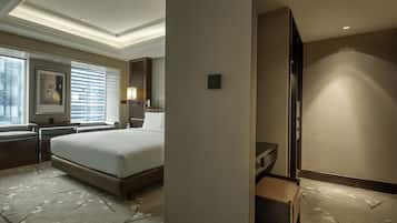 A hotel room with a large bed, a desk with a lamp, a chair, a small table, and a window with blinds.