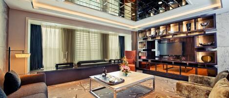 A modern living room with a large window, a flat-screen TV, a coffee table, and a bookshelf.