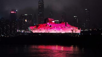Un edificio moderno con un diseño angular único, iluminado con luces rosas que se reflejan en el agua.
