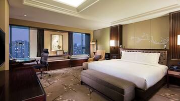A hotel room with a large bed, a desk, a chair, a TV, and a view of the cityscape.