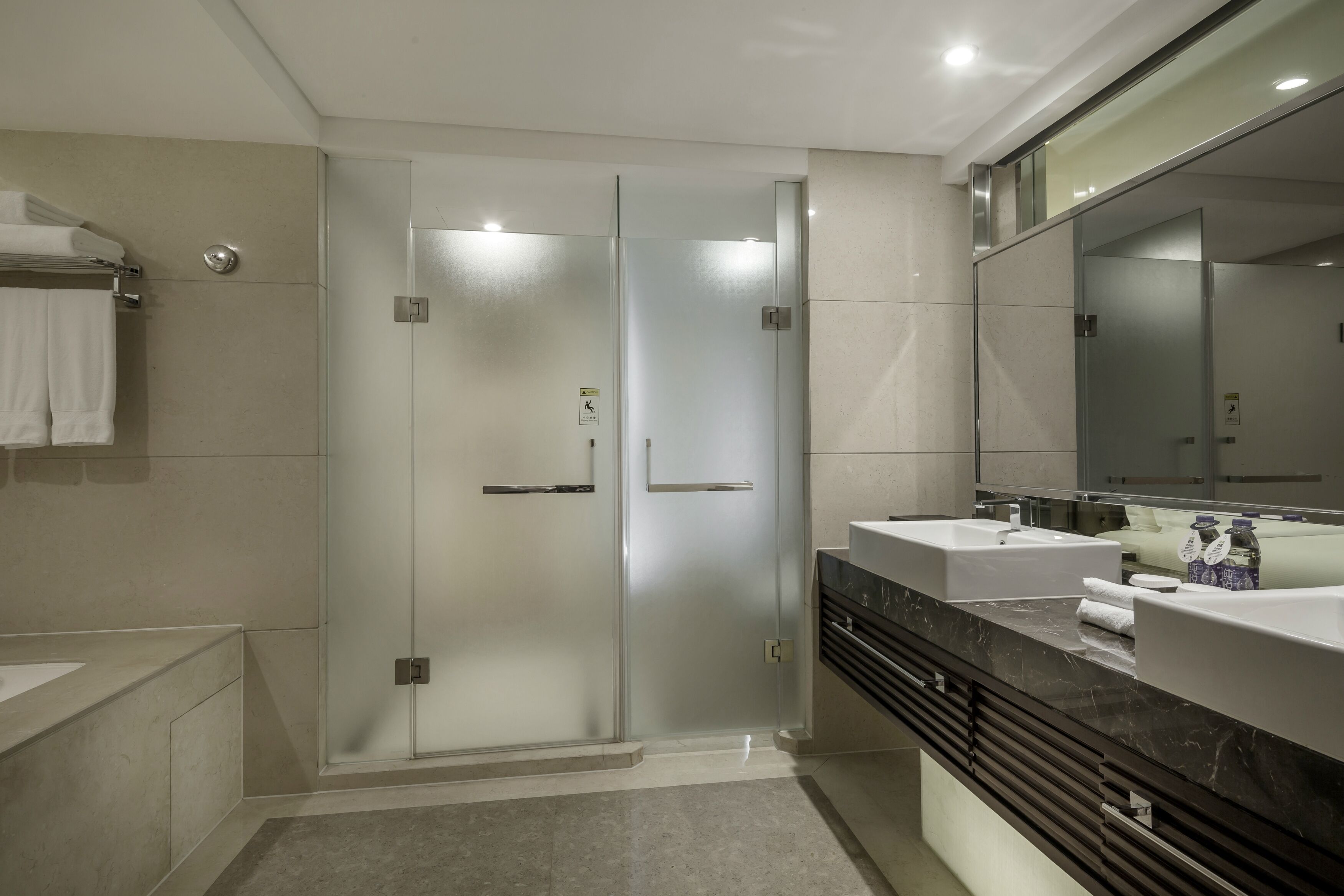 Une salle de bain moderne dotée d’une douche à parois de verre, de deux vasques et d’un grand miroir.