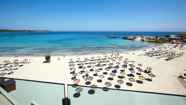 A beach with numerous umbrellas and sun loungers, a lifeguard tower, and a clear view of the sea. - Universal Hotel Perla (Sant Llorenc des Cardassar)