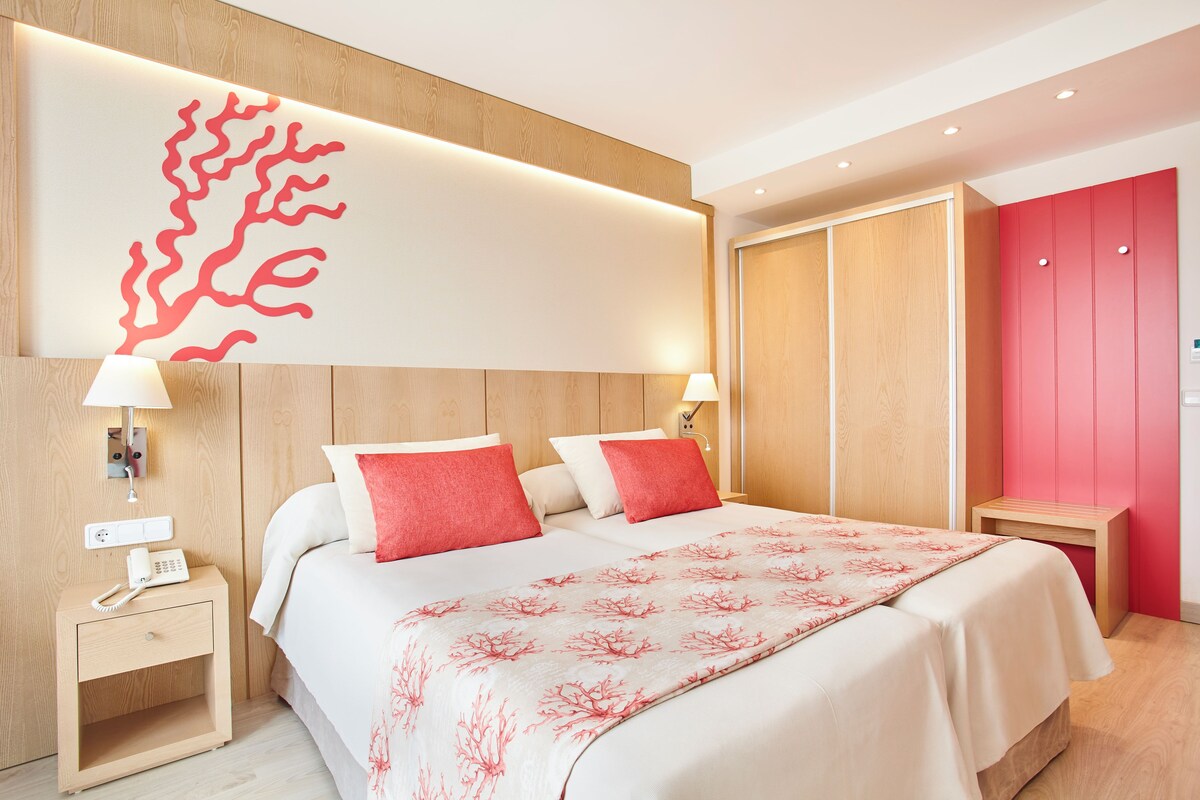 A hotel room with a bed, bedside tables, a phone, and a wall with a coral-like design.