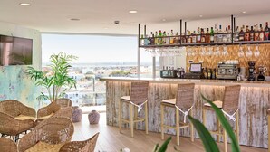 A modern bar area with wicker chairs, a bar counter, and a view of the city. - Universal Hotel Perla (Sant Llorenc des Cardassar)