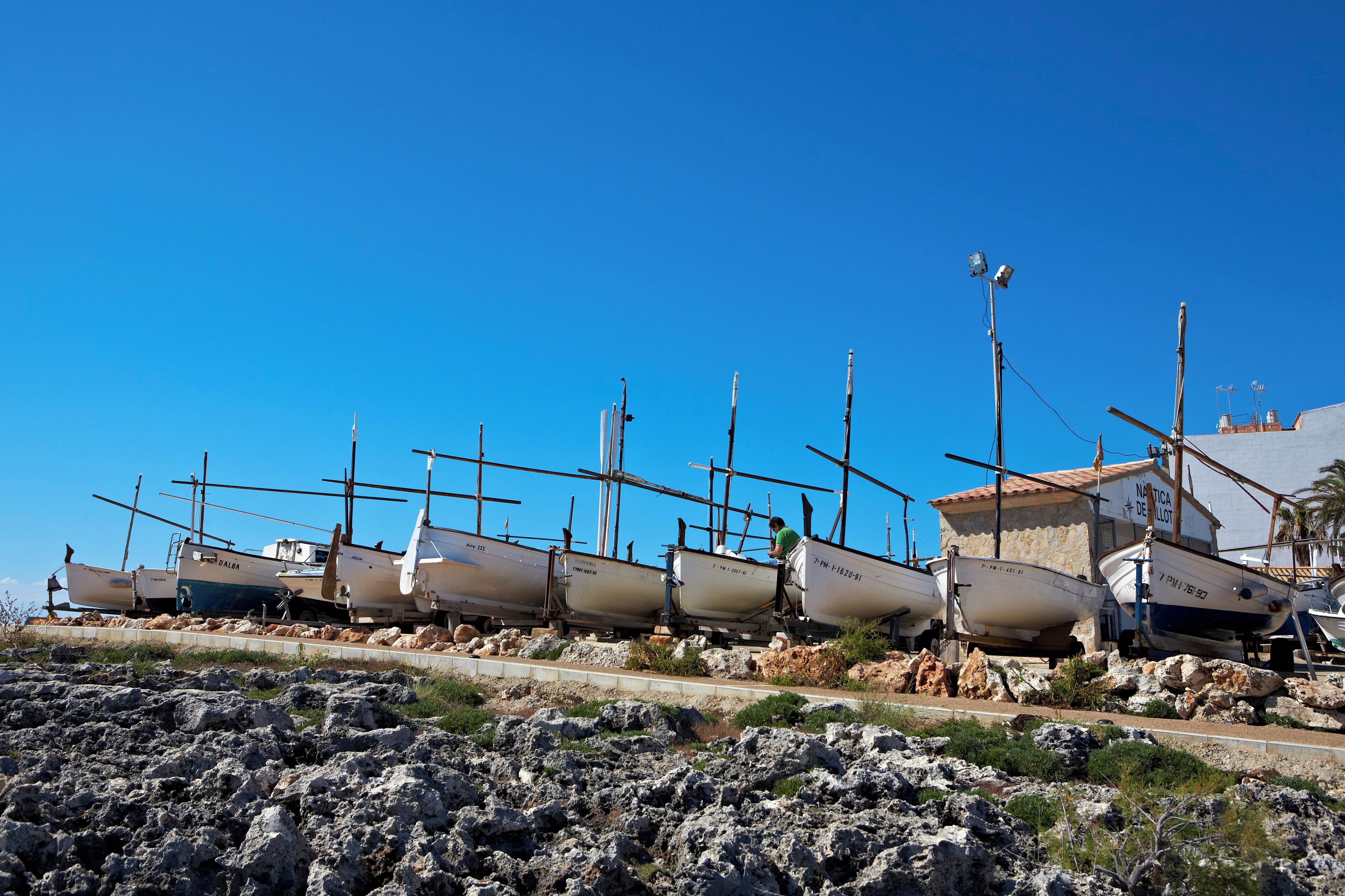 A row of boats docked on a rocky shore with a clear blue sky.