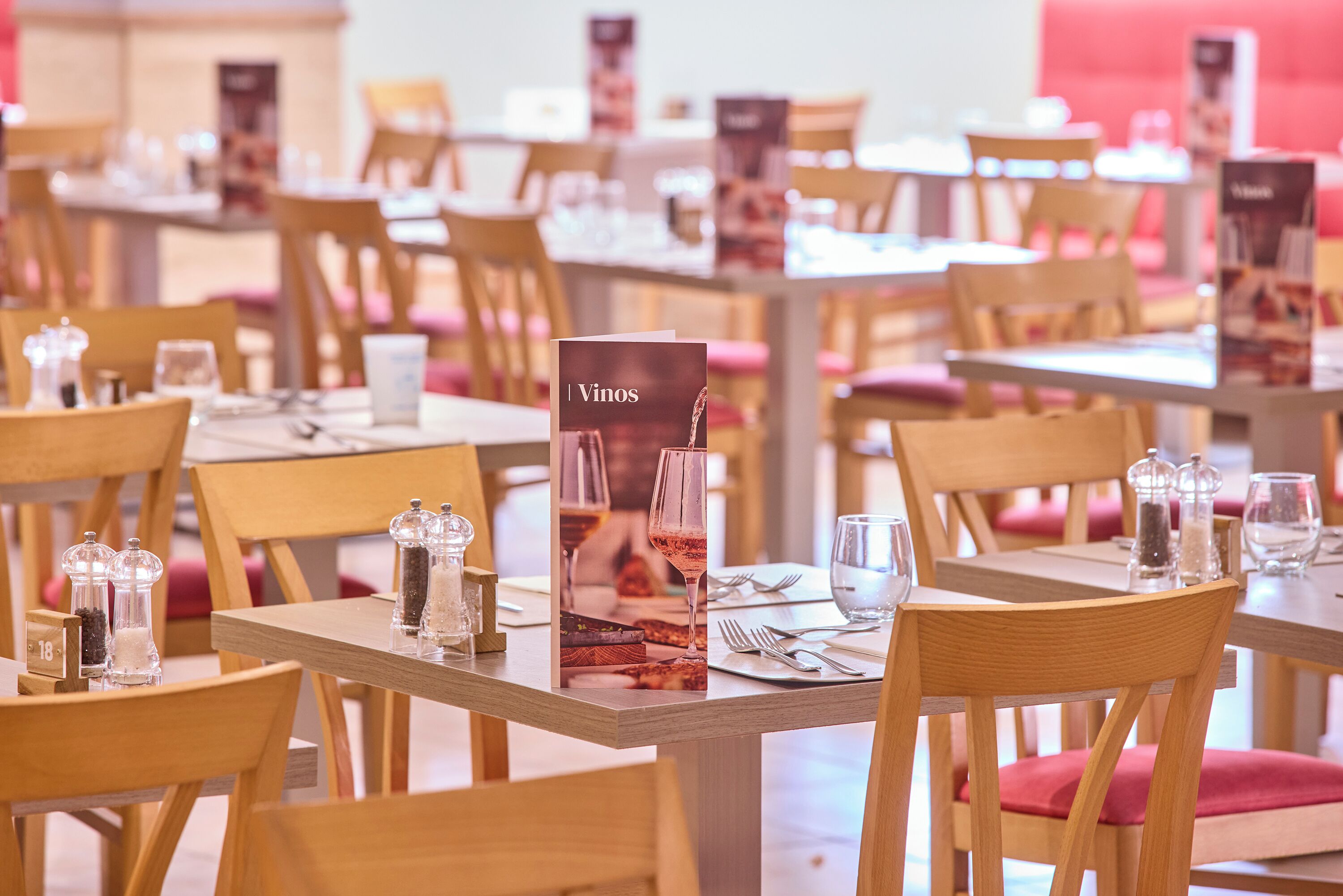 Interior de restaurante con mesas y sillas de madera, menús y cristalería.