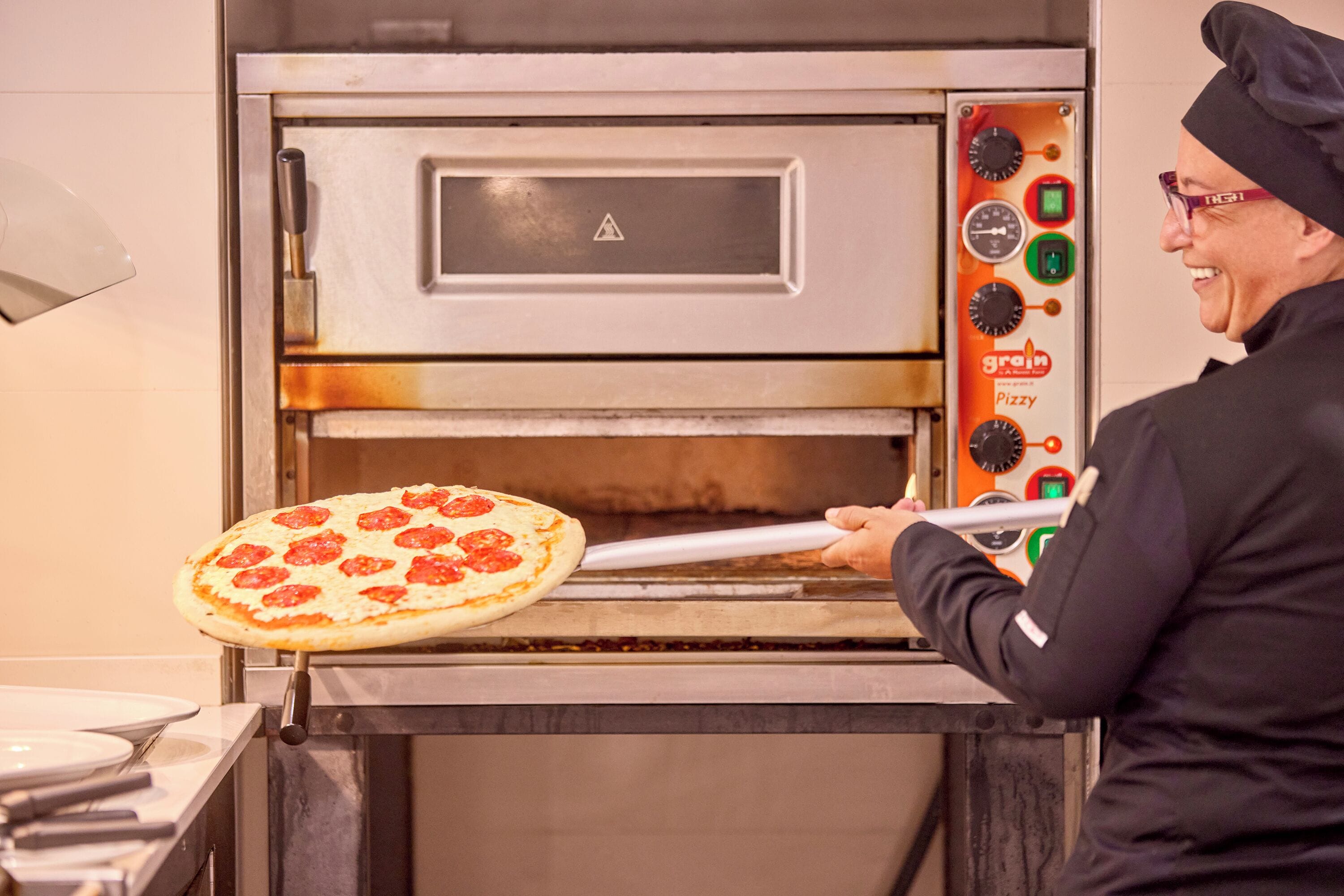 A pizza oven with a control panel and a person holding a pizza.