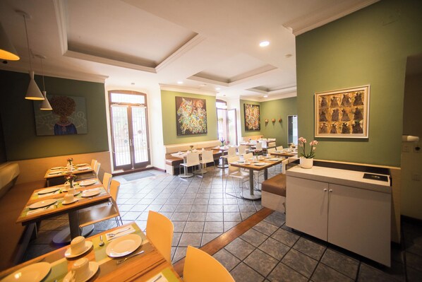 A restaurant with multiple dining tables and chairs, a kitchen area, and artwork on the walls.