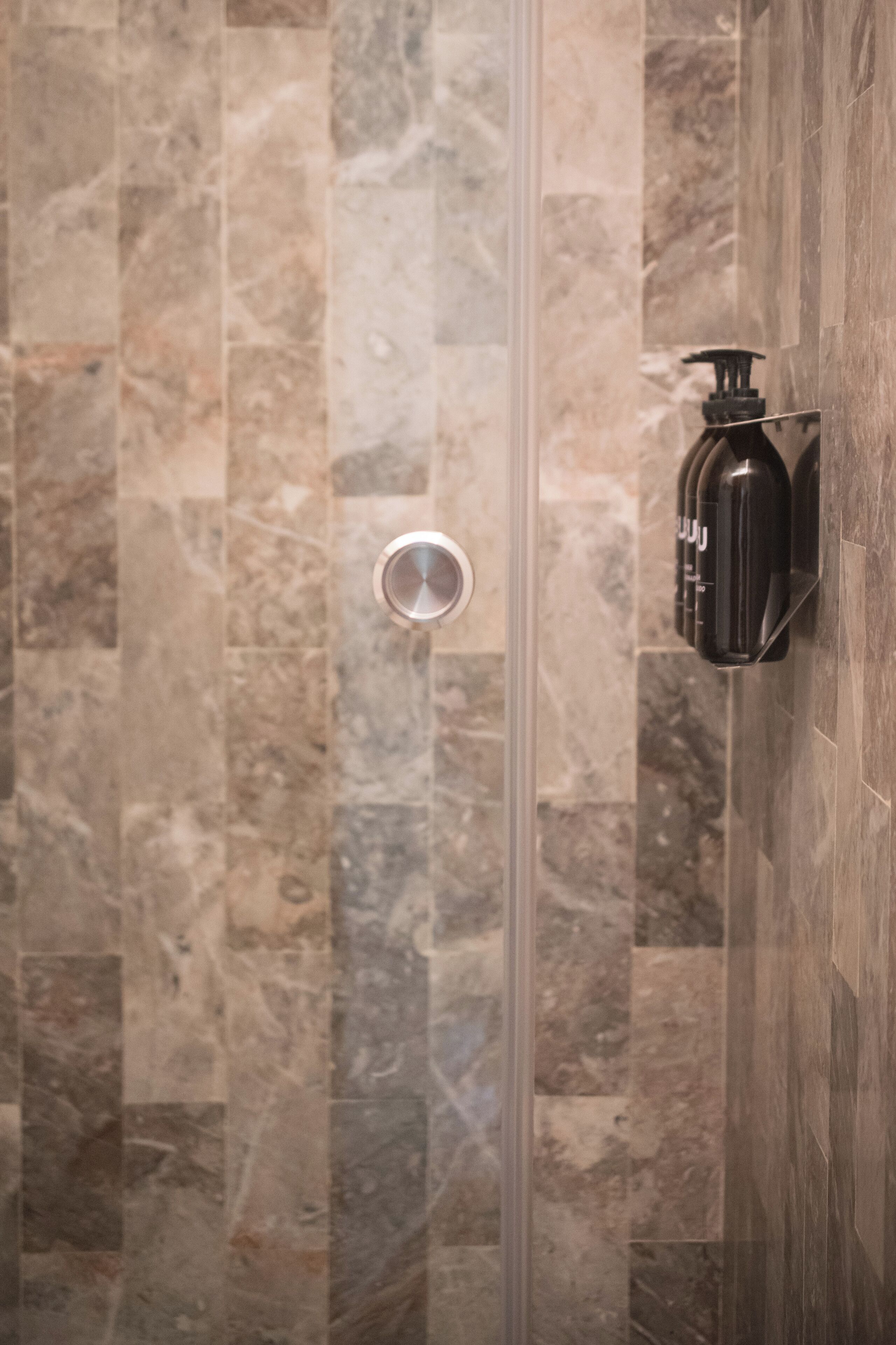 A shower area with a glass door and a wall-mounted soap dispenser.