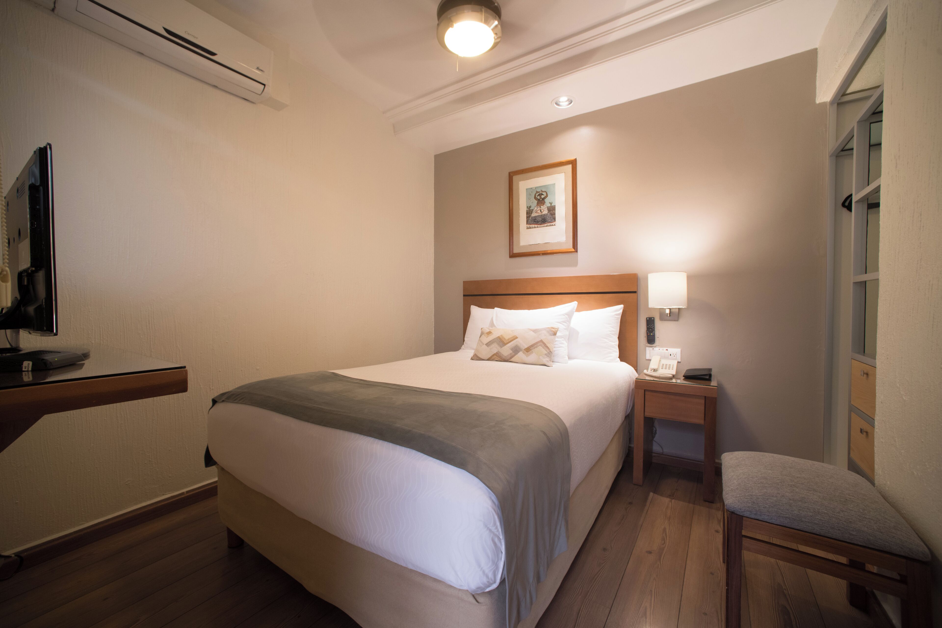 A hotel room with a bed, bedside table, lamp, chair, and a framed picture on the wall.
