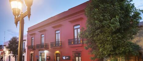 A red building with balconies, a tree in front, and street lamps.