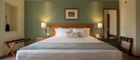 A large bed with a wooden headboard, two bedside tables with lamps, a framed picture above the bed, and a mirror on the wall.