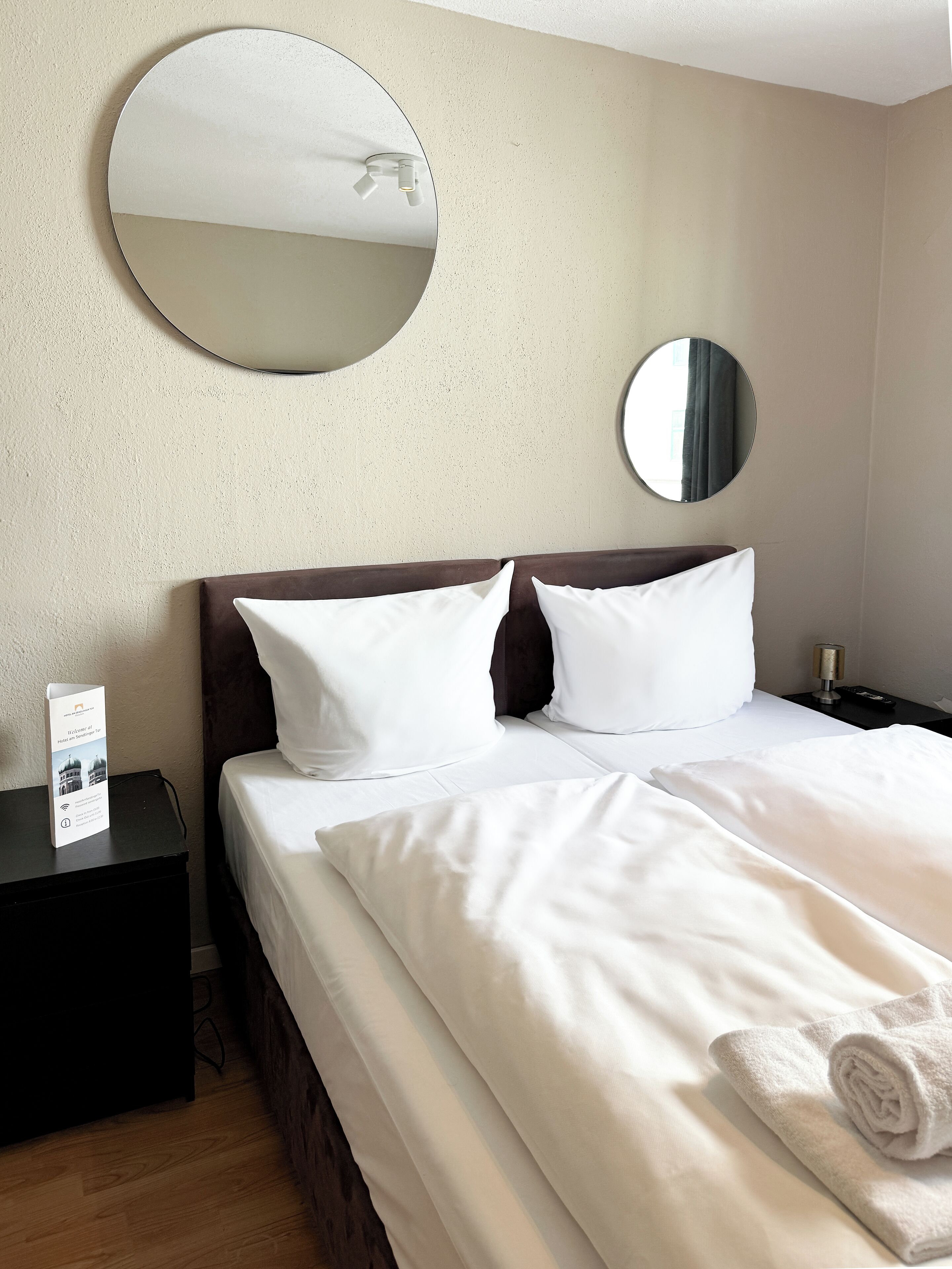 Una habitación de hotel con una cama, dos almohadas, una mesita de noche, un espejo y una toalla.