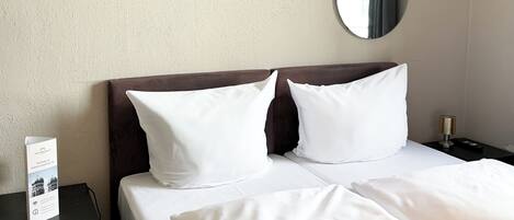Una habitación de hotel con una cama, dos almohadas, una mesita de noche, un espejo y una toalla.