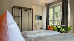A hotel room with a bed, a TV mounted on the wall, a window with curtains, and a table with chairs. - Hotel am Sendlinger Tor (Munich)