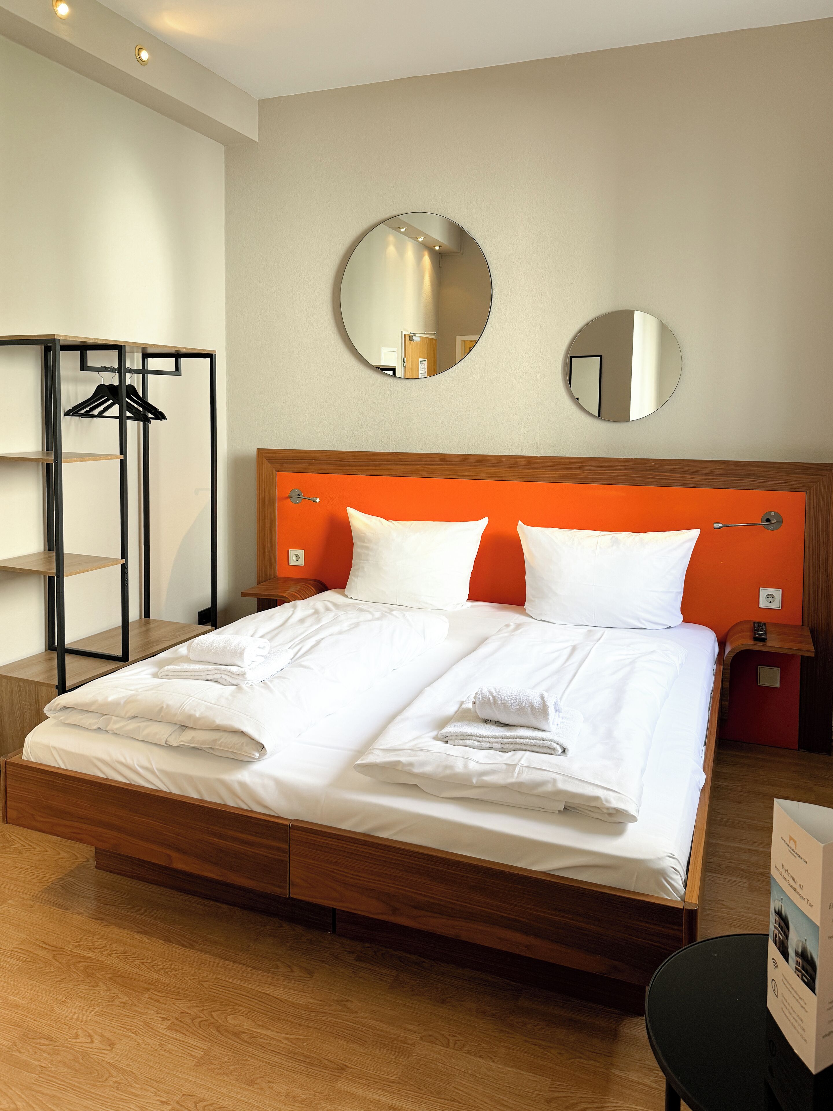 Een keurig opgemaakt bed met witte lakens, een houten hoofdbord en twee nachtkastjes met lampen.