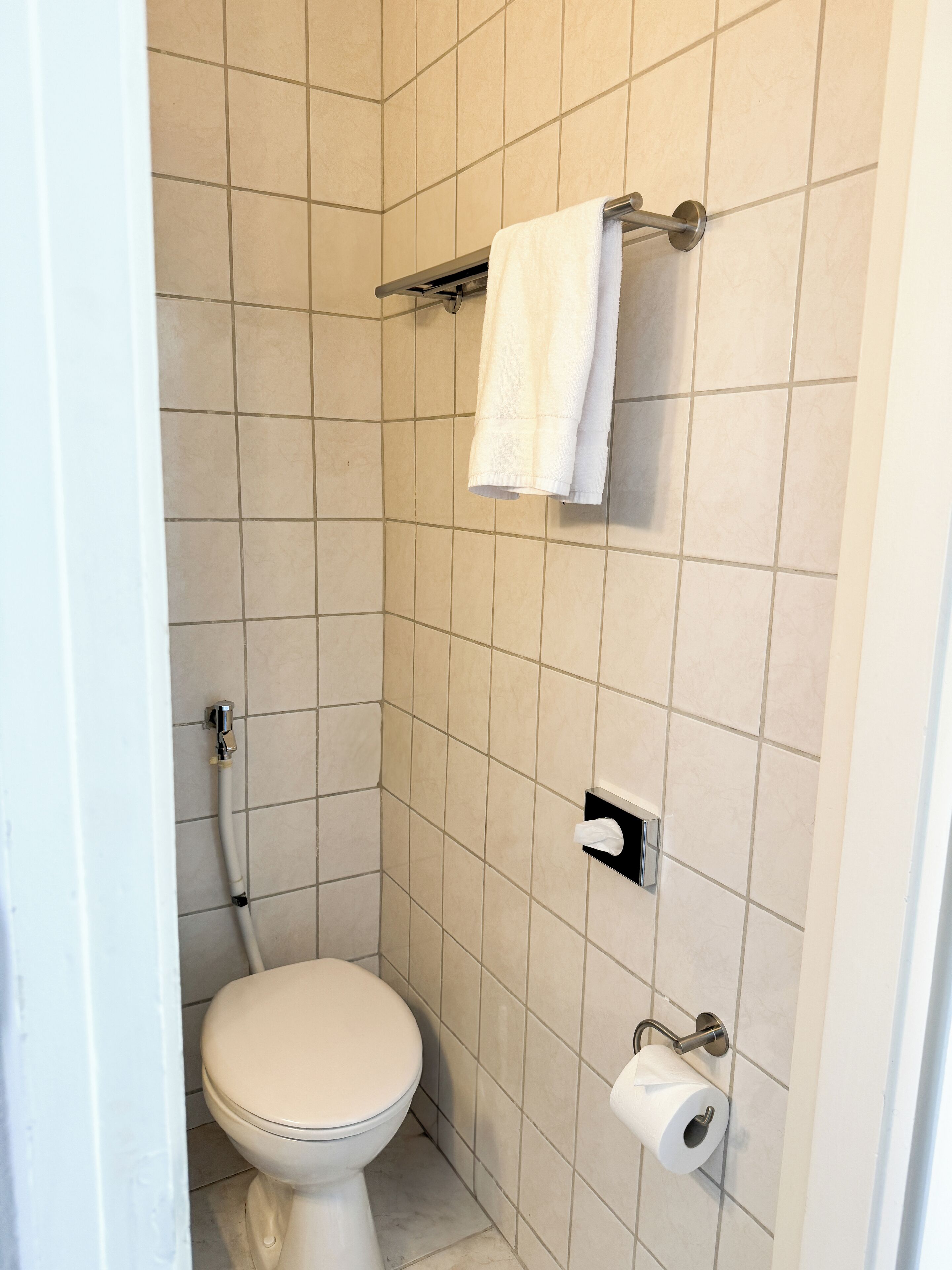 A small, tiled bathroom with a toilet, a towel rack, and a paper towel dispenser.