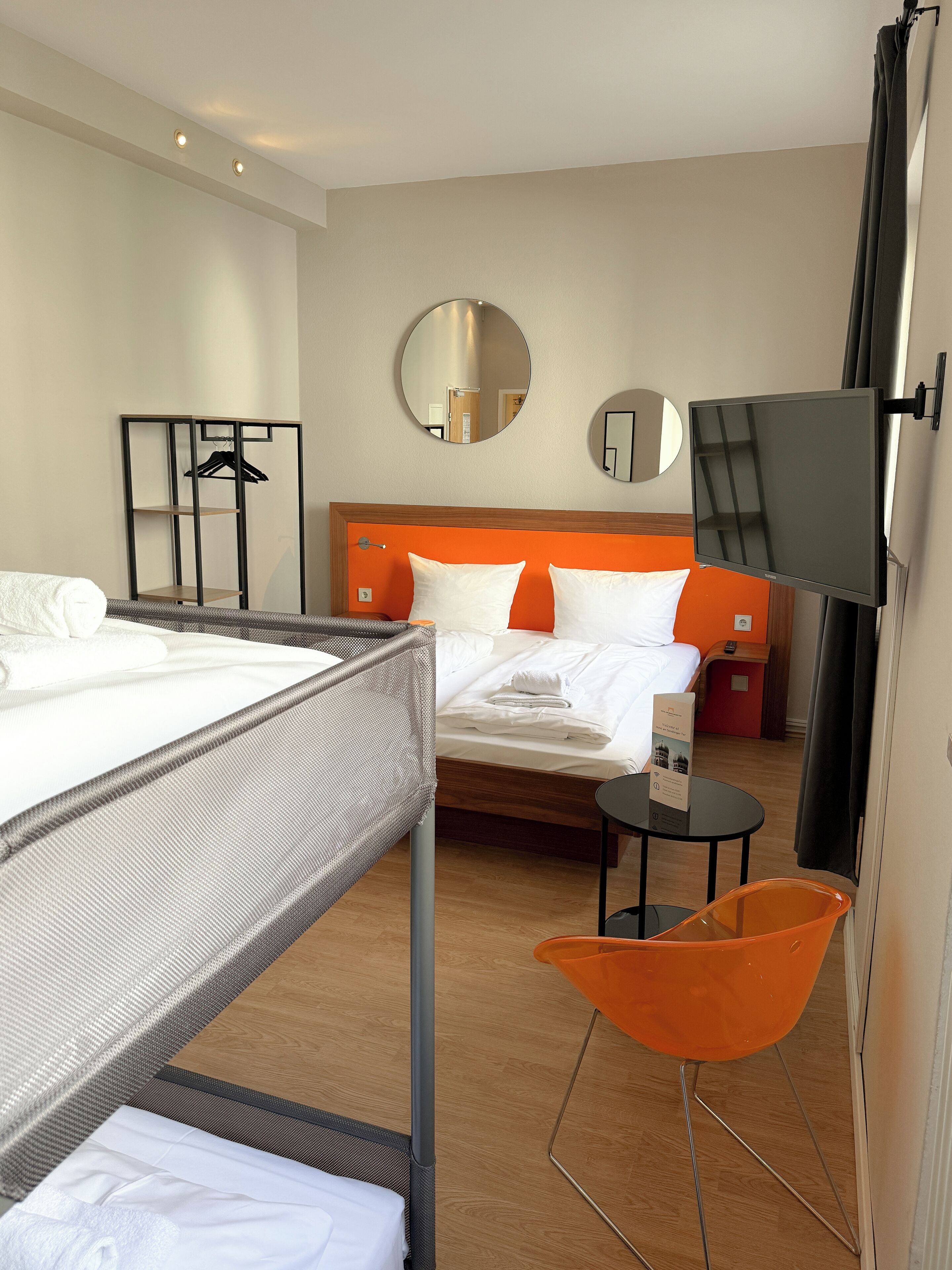 A hotel room with a bed, a desk, a chair, a TV, and a mirror.