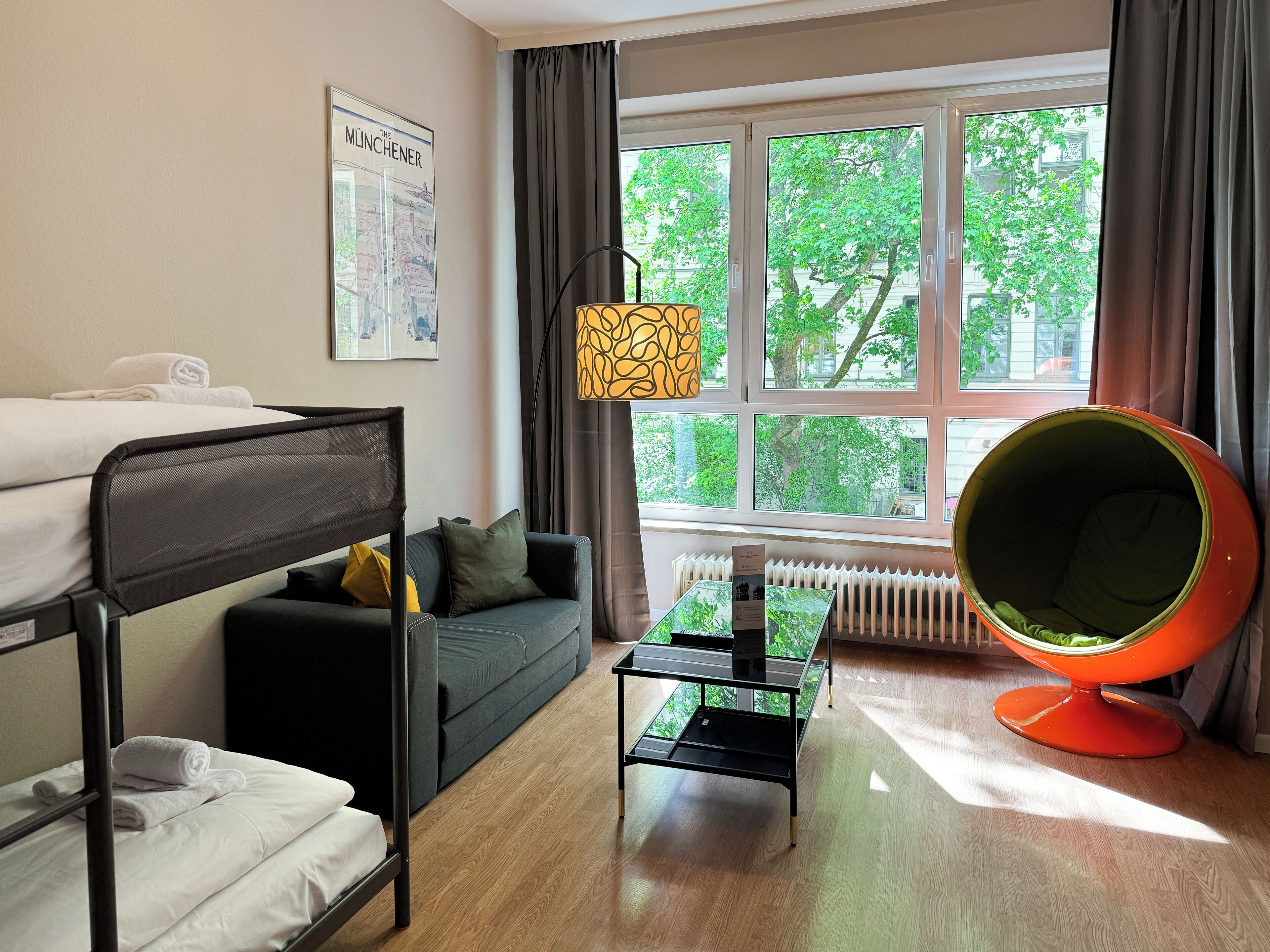 Ein Zimmer mit einem Etagenbett, einer Schlafcouch, einem Tisch, einem Stuhl und einem fenster mit Vorhängen.