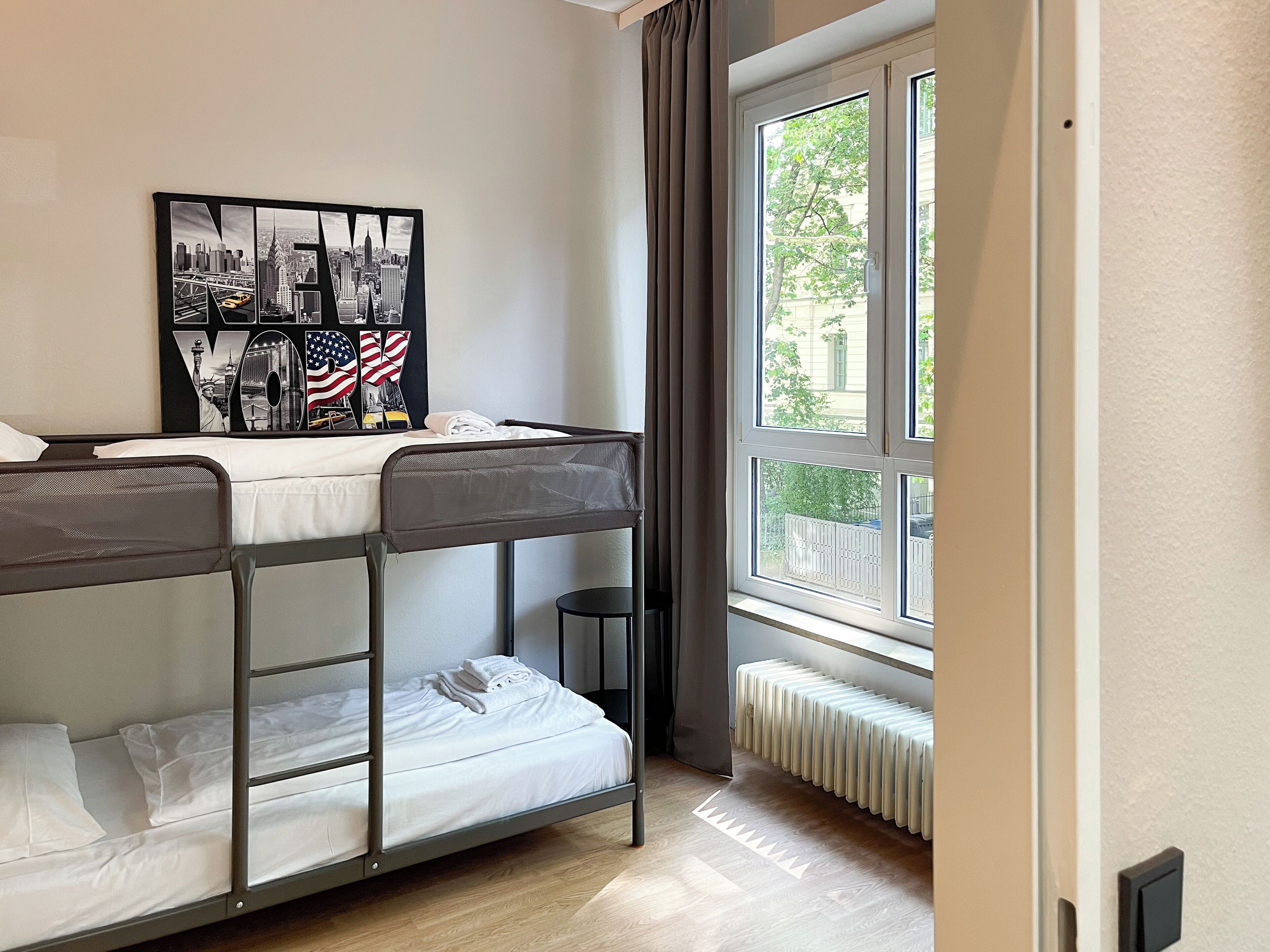 Habitación con literas, un cartel de paisaje urbano, una ventana con cortinas y un radiador.
