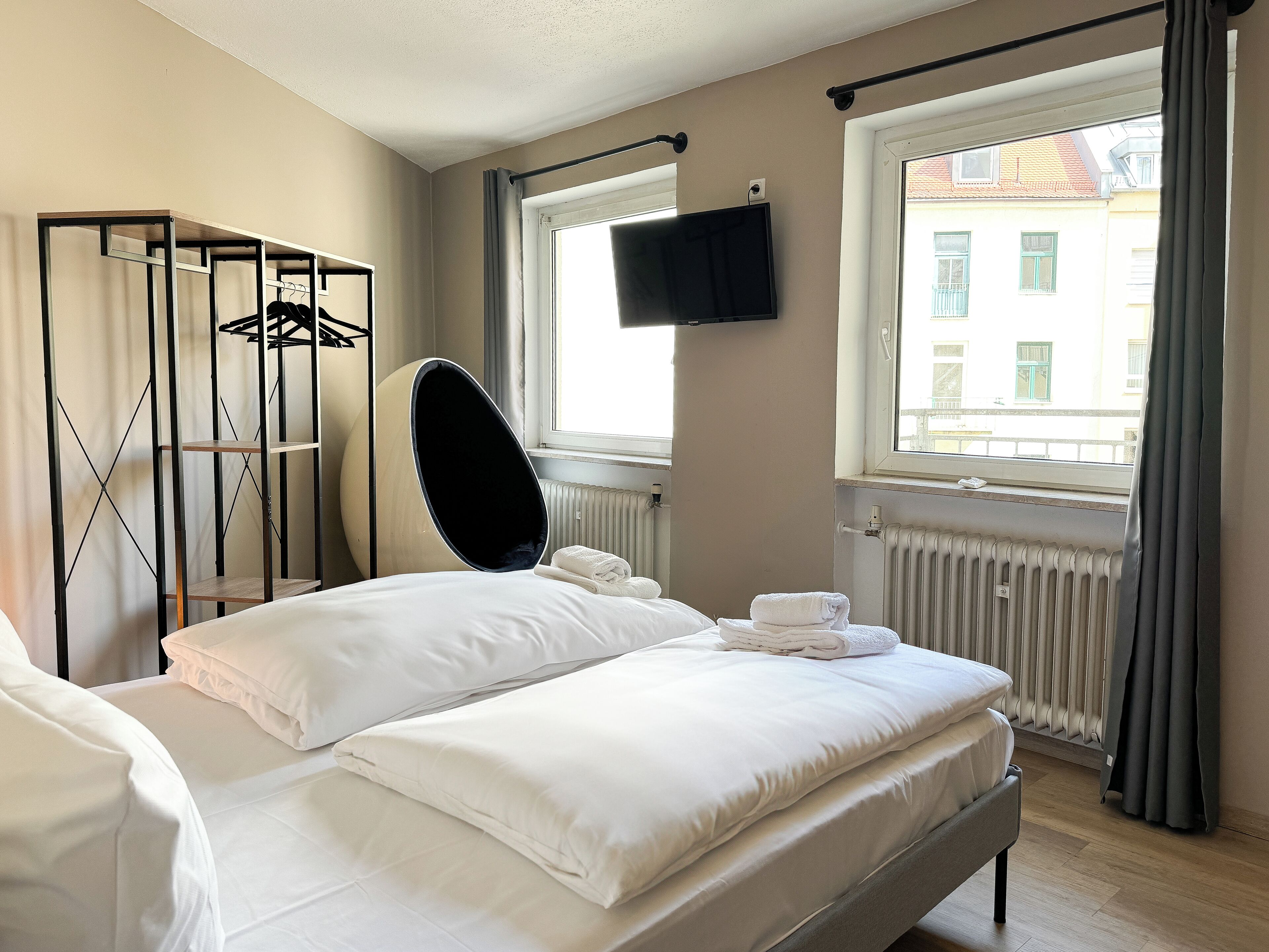 A hotel room with a bed, a hanging chair, a TV, and a window with a view of buildings.
