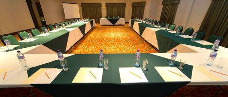 A conference room with long tables, green chairs, water bottles, and nameplates.