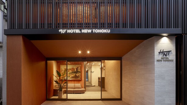 The entrance of the HNT Hotel New Tohoku with a modern design, featuring a wooden facade, a glass door, and a sign above the entrance. - Hotel New Touhoku (Tokyo)